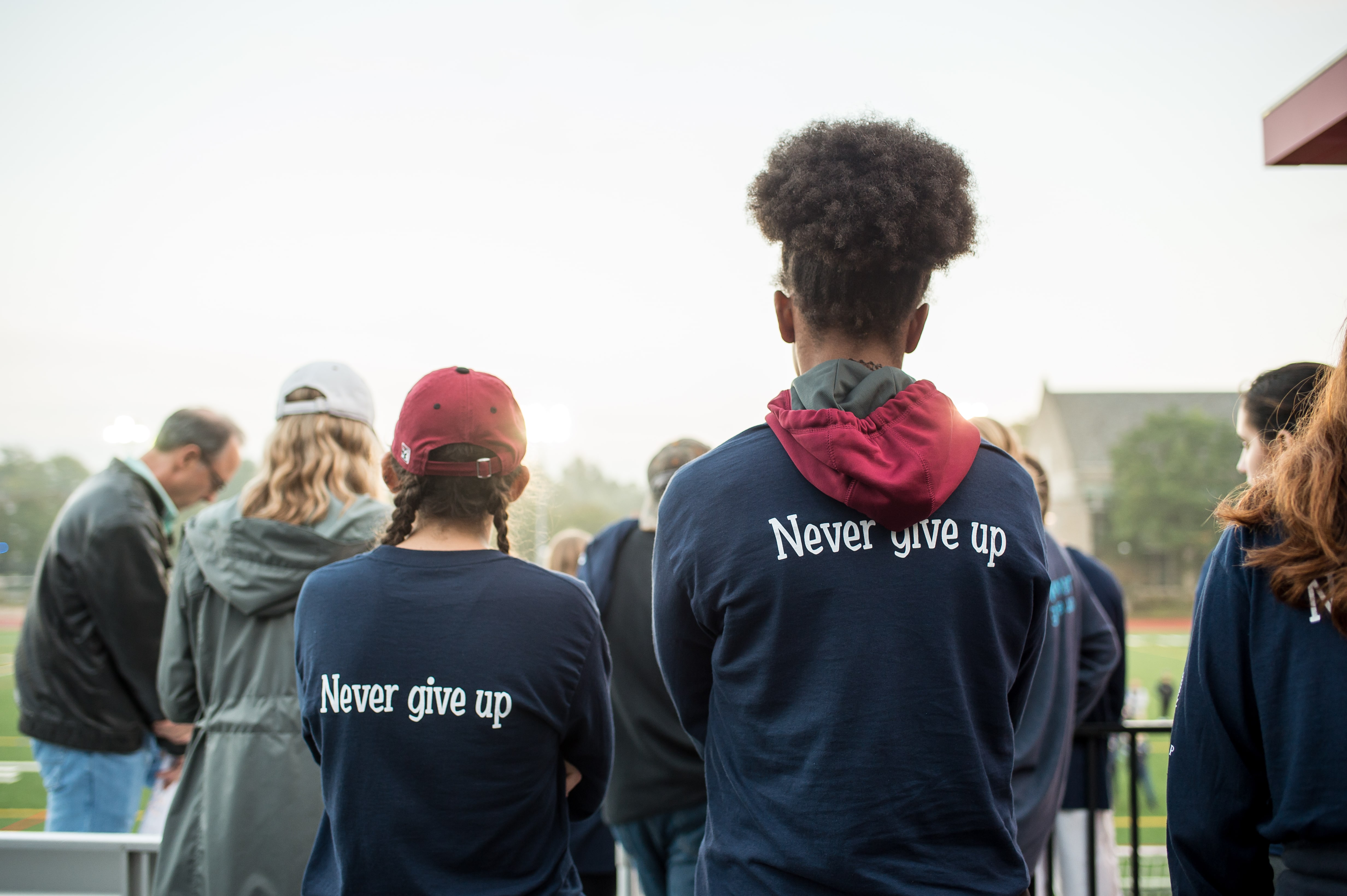 Two students stand with their backs to the camera with 'never give up' written on the backs of their shirts
