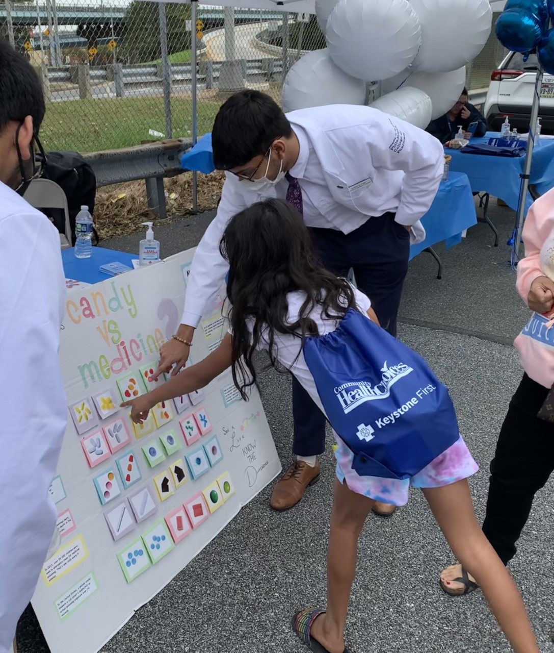 A USciences pharmacy student explains a chart titled "Medicine vs Candy" to a young girl