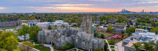 The green campus of Hawk Hill, Saint Joseph University's main campus, the gothic spires of Barbelin Hall rise in the foreground and the skyscrapers of Philadelphia loom in the background
