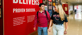 two students walking in hallway with 'Haub Delivers' sign and photos on the wall