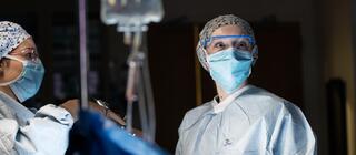female nurse in hospital room wearing mask, scrubs and glasses