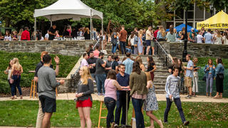 A large group of people mingles on the lawn with tents behind them for the activities.