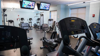 A fitness center inside a residence hall with ellipticals and televisions