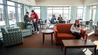 A common study area with desks, couches and big windows. Students working and socializing.
