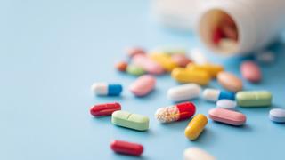 Colorful pills scattered from white plastic pill bottle on blue background