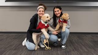 Two female students kneel down with their dogs