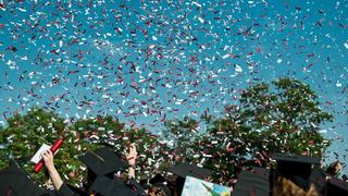 Red and white confetti in the sky above a group of graduates in caps and gowns