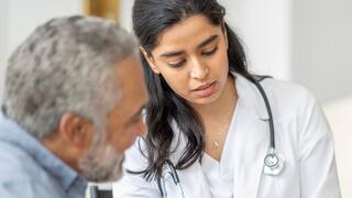 Nurse wearing a white lab coat and stethoscope pointing to a clipboard and explaining results to a patient