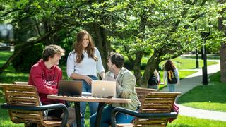 Saint Joseph's students sitting at bench outside during spring 