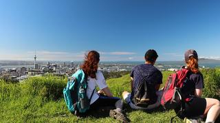 Three students sit on a hill overlooking Auckland, New Zealand