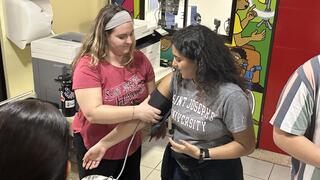 A photo of a college student showing how to use a blood pressure reader on another student.