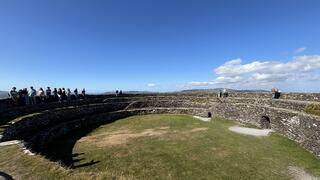 Students visiting Ring Fort in Northern Ireland. It is a clear, blue sky with bright green grass and a stone fort ring.