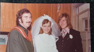 Woman wearing wedding dress standing beside husband and friend