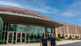 Two students walking away from a large modern nursing school building
