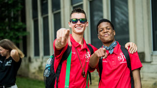 Two students smiling and pointing at the camera