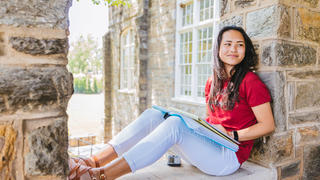 A woman sits in a window sill with a book in her lap