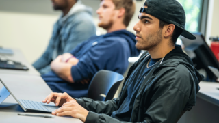 male student in the classroom with his hands on his laptop