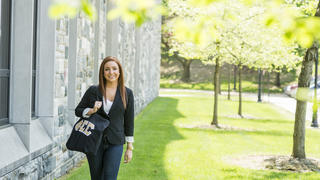 A woman smiles carrying a tote bag with greek lettering for a sorority