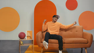 Kevin Carroll '97, author of the Rules of the Red Rubber Ball, smiling and sitting on an orange couch