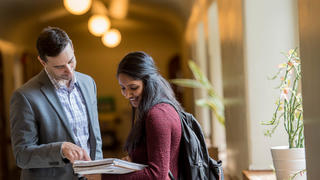 A teacher and student look at a book together in a hallway