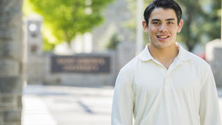 Chris Blewitt stands outside on campus on a spring day with the Saint Joseph's University sign in the background