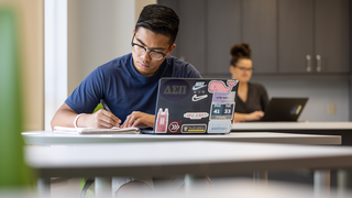 male saint joseph's university student writing on a notebook inside a classroom