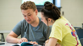 Two college students talking to each other inside a classroom at Saint Joseph's University