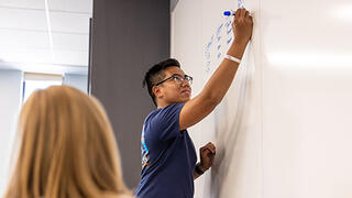 Students in classroom writing on white board.