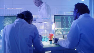 White coat scientists working at a desk that has a computer running complex calculations