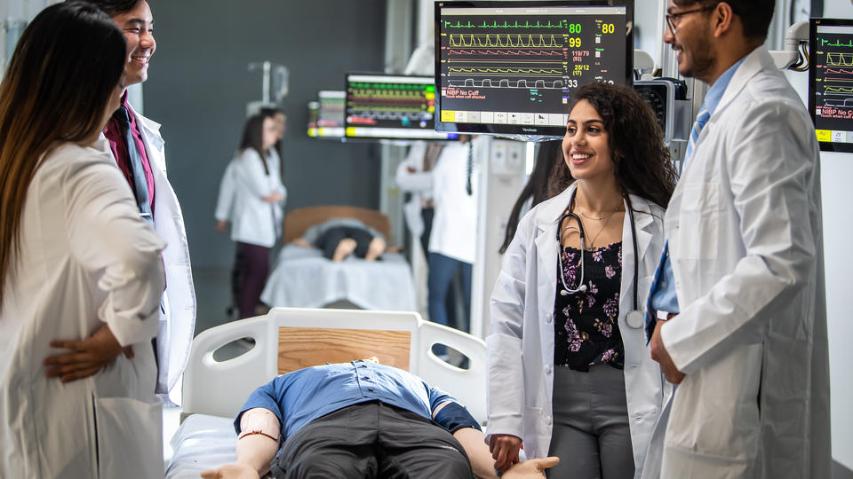 A group of Saint Joseph's health professional students dressed in white coats work in a simulated hospital setting