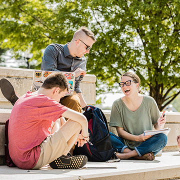 three students sitting outside and doing class work together