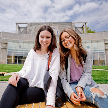 two female saint joseph's university students sitting next to each other outside