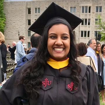 Elisa smiles at the camera wearing her graduation cap and gown