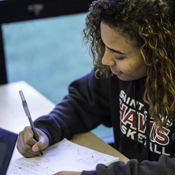 A woman in a HAWKS sweatshirt writes in her notebook.