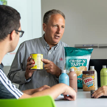 Professor holding a potato chip bag and cans of food while teaching students