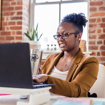 Woman sitting behind her laptop using SJU cup in office