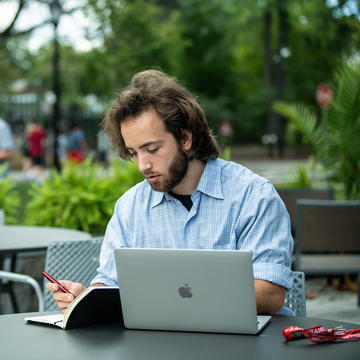 Saint Joseph's University student sitting on a table outside on his laptop