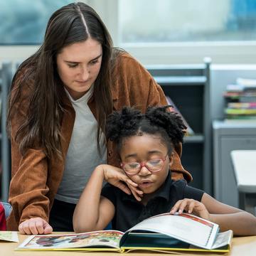 Saint Joseph's University Gompers student teacher helping student read a book in class