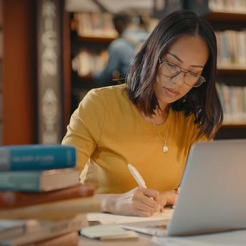 Female student working on laptop and writing on notebook