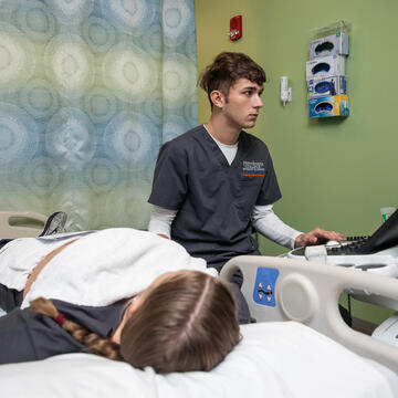 Student looking at an ultrasound screen with patient lying on table