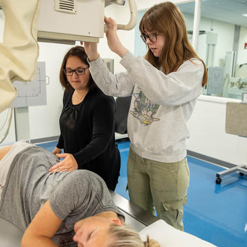 Student laying on radiation table with another student positioning radiation machine