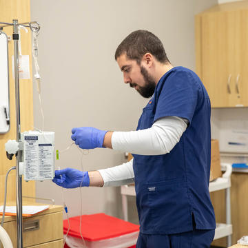 Male nurse filling an IV bag beside patient's bed