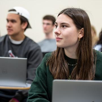 Students sitting in a classroom with laptops listening to a professor