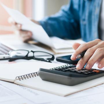 Zoomed in image of fingers typing on a calculator and holding papers