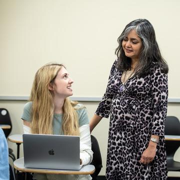 Student speaking with a professor while sitting at a desk in front of a laptop