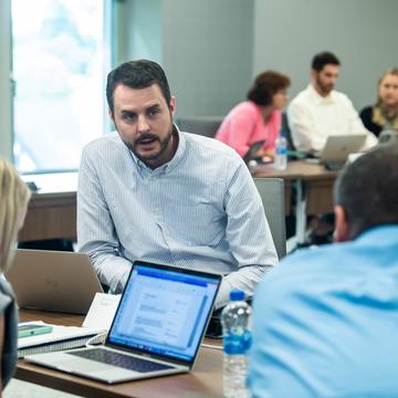 Student conversing with other students in a classroom with a laptop open on the desk