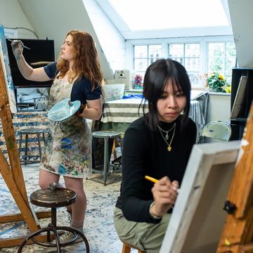 Two art students painting on canvas in an art classroom