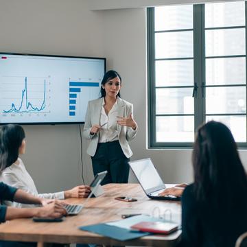 Woman leading a business meeting while standing in front of a presentation screen with charts and graphs