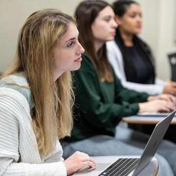 Student listening to professor in a classroom with laptop open