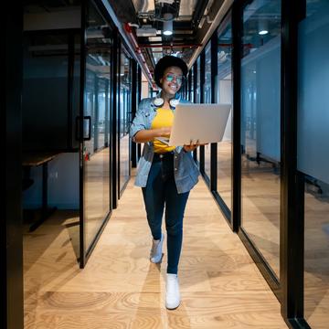 Woman holding computer while walking through a room full of IT servers